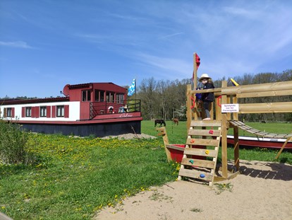 Rollstuhlgerechte Unterkunft - Unterkunftsart: Ferienwohnung - Blick von der Terrasse auf das Filmschiff ERBSE und den Spielplatz nur für das Erdhaus und das Filmschiff - Erdhausapartment WEST